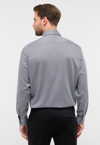 Camicia da uomo a maniche lunghe in navy con piccolo motivo geometrico, polsini con bottone e colletto classico. Realizzata in tessuto morbido, vestibilità aderente.