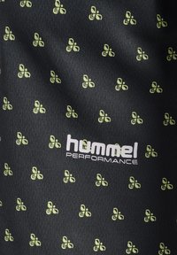 Svart sporttyg med ett upprepat mönster av små gröna former; inkluderar "hummel PERFORMANCE"-logotyp i vitt.