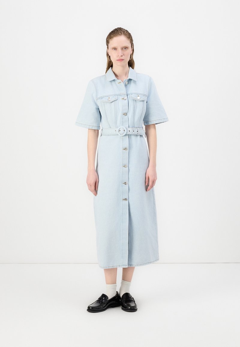 Lyseblå denimkjole med korte ermer, belted midje, knappelukking og to brystlommer. Brukt sammen med svarte sko og hvite sokker.