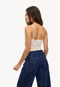 Camisola de encaje en crema con tirantes finos, combinada con unos vaqueros de pierna ancha de talle alto en azul oscuro que cuentan con dos bolsillos traseros y costuras visibles.