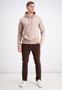 Bež kapučo majica s prednjim žepom, uparena s tamnosmešnim kordura hlačama i belim patikama. Glatka tkanina s opuštenim krojem.