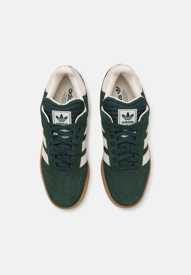 Baskets en suède vert avec des rayures blanches et un col beige. Elles disposent de lacets ronds, d'une languette rembourrée et d'une semelle extérieure en gomme texturée.