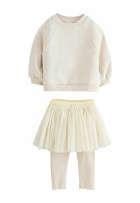 Krämfärgad sweatshirt med raglanärmar, fluffig textur; lager av krämfärgad tylkjol; mjuka beige leggings med vågiga fållar och ribbat mönster.