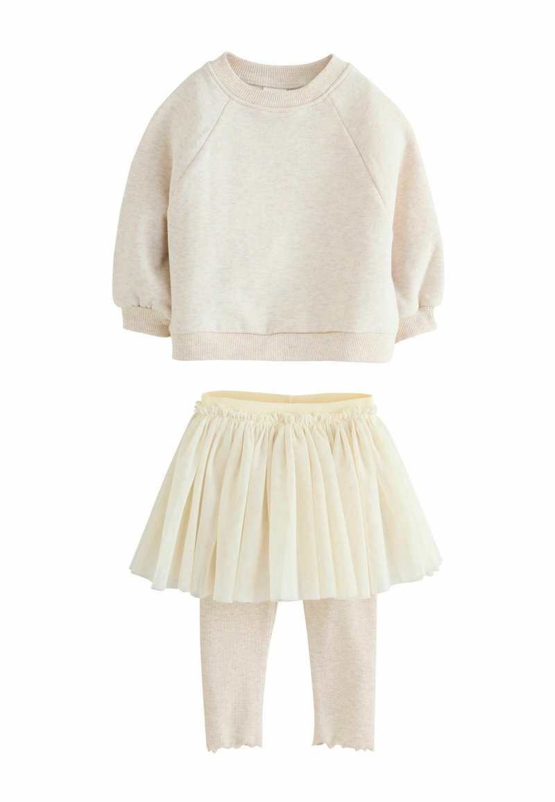 Krämfärgad sweatshirt med raglanärmar, fluffig textur; lager av krämfärgad tylkjol; mjuka beige leggings med vågiga fållar och ribbat mönster.