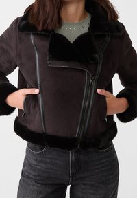 Sort jakke i imiteret pels med læderdetaljer, der har lynlås foran, stor krave og sidelommer. Blød tekstur med ensfarvet design.