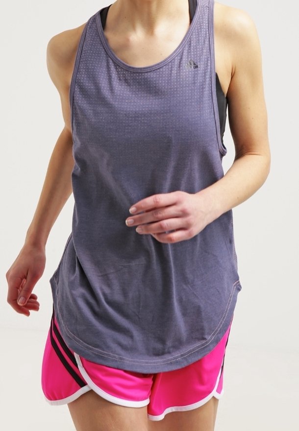 Personne en train de faire du jogging portant un débardeur violet ample et un short de sport rose vif avec un bord blanc sur un fond clair.