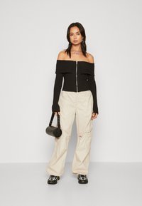 Czarny, prążkowany top typu off-the-shoulder z zamkiem, beżowe luźne spodnie cargo oraz fakturowana czarna torebka. Obuwie ma sportowy design.
