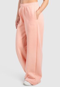 Pantalones de chándal rosa claro hechos de una tela suave, con un corte holgado, cintura elástica, bolsillos y un acento blanco a lo largo de las costuras.