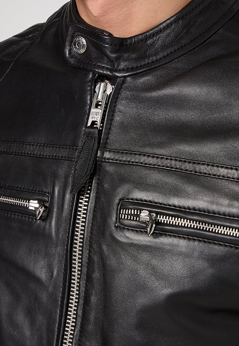 Chaqueta de motocicleta de cuero negro con un alto cuello, bolsillos con doble cremallera y herrajes plateados con detalles de costura visibles.