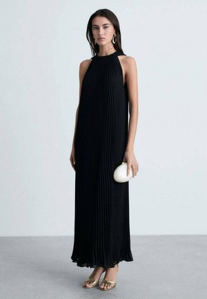 Black pleated maxi dress with a high neckline, sleeveless design, and flowing silhouette. Paired with a cream clutch and gold sandals.