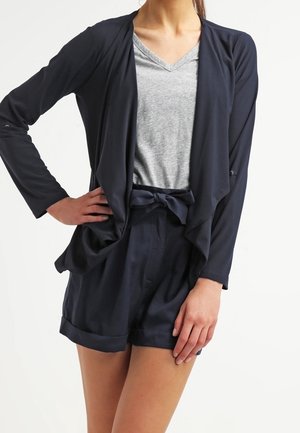Cardigan aperto blu navy, top grigio a scollo a V e pantaloni corti abbinati blu navy con vita legata. Tessuto morbido e liscio, vestibilità rilassata e maniche arrotolate.