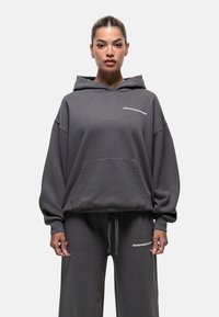 Felpa grigia con tasca frontale e cappuccio regolabile, con il testo "GOODFORNOTHING" sul petto. Pantaloni sportivi morbidi e dalla vestibilità rilassata che completano il look.