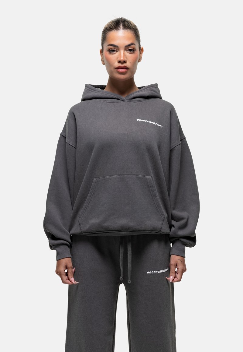 Felpa grigia con tasca frontale e cappuccio regolabile, con il testo "GOODFORNOTHING" sul petto. Pantaloni sportivi morbidi e dalla vestibilità rilassata che completano il look.