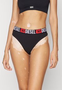 Bikini noir en coton avec une ceinture logo "DIESEL" rouge et blanche. Il présente une texture lisse et un design classique taille haute.