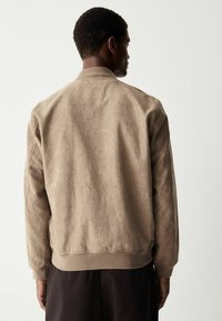 Beige bomberjakke med en glat tekstur, ribbet krave og manchetter samt en afslappet pasform, vist fra ryggen mod en neutral baggrund.