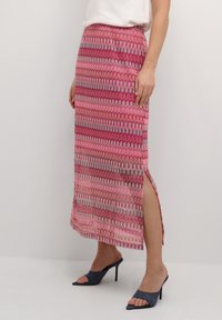 Maxi sukně s vlnkovým vzorem v odstínech růžové, červené a šedé, s bočním rozparkem a hladkou texturou látky, v kombinaci s vysokými podpatky.