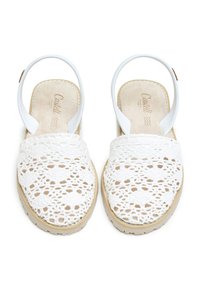 Sandalias blancas de ganchillo con patrón, de espalda abierta, con suelas beige y correas en el tobillo blancas, vistas desde arriba.