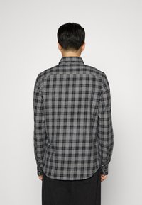 Camisa de manga larga a cuadros grises con cuello abotonado, dobladillo curvado y patrón de cuadros en blanco y negro en tela suave.