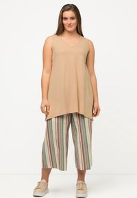 Top beige senza maniche con scollatura a giro, abbinato a culotte a lunghezza ginocchio a righe multicolori nei toni pastello, indossato con sneakers beige chiaro.