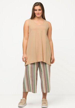 Haut sans manches beige avec un col en forme de U, associé à des culottes mi-genoux à rayures multicolores dans des tons pastel, portées avec des baskets beige clair.