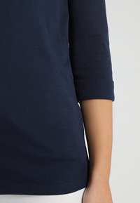 Mörkblå bomulls-T-shirt med trekvartslånga ärmar och uppvikta muddar. Slät textur och enkel design med rak nederkant.