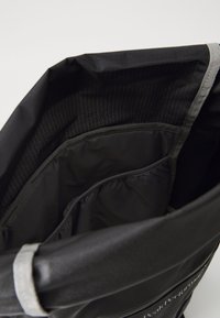 Black fabric bag with a structured shape, featuring a smooth inner lining and side pockets. Dull silver accents along the edges.
