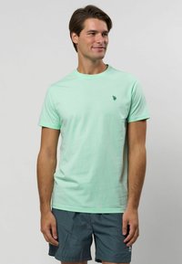 Mátově zelené bavlněné tričko s krátkými rukávy a kulatým výstřihem, s malým tmavě zeleným logem na levé části hrudníku.