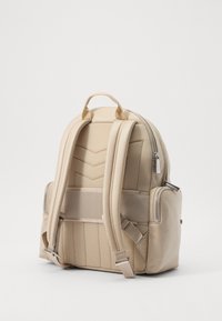 Zaino in tessuto beige con superficie strutturata, motivo a zigzag sul retro, spallacci imbottiti e tasca laterale con zip.