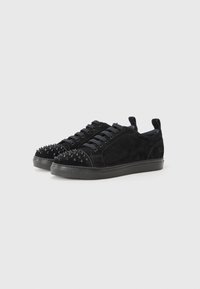 Black suede sneakers featuring a rounded toe, flat laces, spike accents on the toe, and a textured rubber sole.