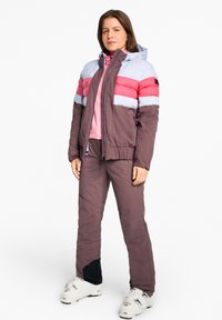 Padded winter jacket with light blue, pink, and red horizontal stripes, paired with matching brown pants and ski boots. Features a hood and zippers.