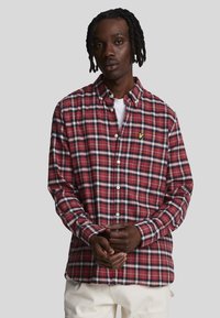 Camicia a quadri rossa e blu navy con colletto button-down, maniche lunghe e bottoni bianchi. Presenta un piccolo logo giallo sul lato sinistro del petto.