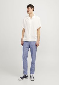 Camisa blanca de manga corta con un patrón texturizado, combinada con pantalones de lino azul claro y zapatillas negras con acentos en blanco.