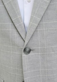 Blazer de cuadros grises con una tela texturizada, que presenta un cierre de dos botones y un detalle de botón blanco único en el frente.