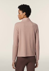 Maglione di un rosa morbido, con colletto alto, maniche lunghe e una vestibilità rilassata. Il tessuto appare strutturato e caldo.