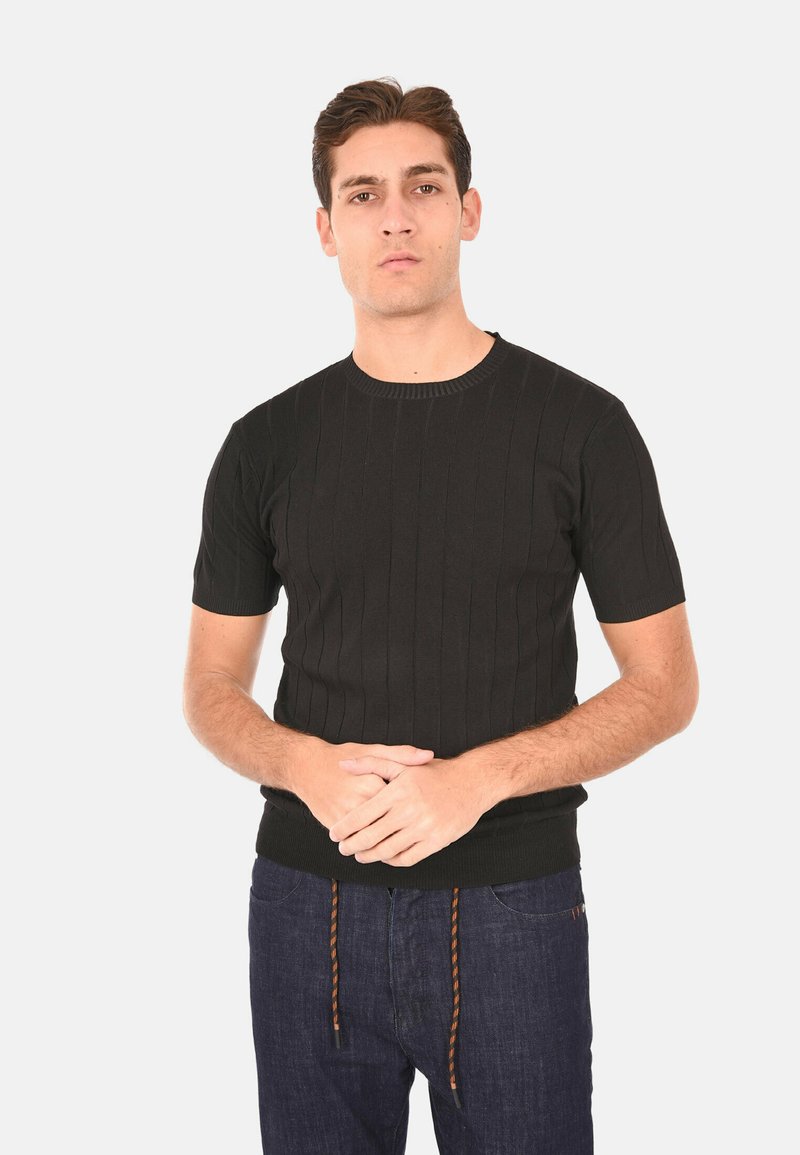 Maglione nero a maniche corte in un design aderente, con scollatura rotonda e tessuto testurizzato. Abbinato a jeans in denim scuro.