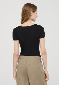 Body nero a maniche corte con scollo rotondo, realizzato in tessuto morbido. Abbinato a pantaloni beige chiaro a vita alta con tasche posteriori.
