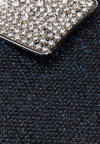 Metallisk accessoar med en texturerad svart tygbakgrund, prydd med ett silveröverdrag dekorerat med många klara rhinstenar i olika storlekar.