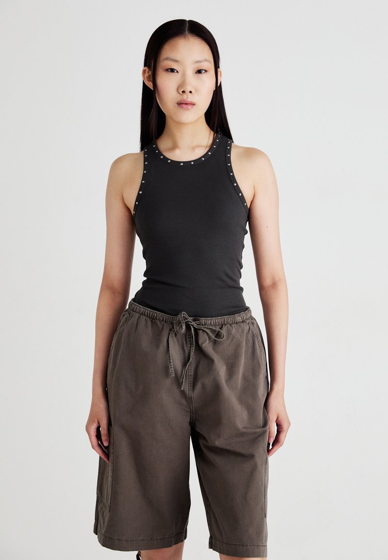 Débardeur gris foncé à côtes avec des clous argentés le long de l'encolure, associé à un short cargo brun ample avec une ceinture élastique et un cordon de serrage.