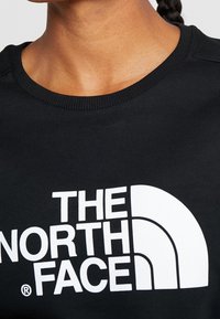 Persona vistiendo una camiseta negra de cuello redondo con un gran logo blanco de "THE NORTH FACE" en el pecho.