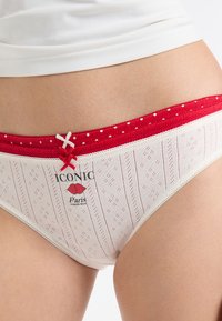 Weiße Baumwoll-Panties mit einem roten, gepunkteten Bund, vertikalen Streifen, dekorativen Schleifen und einem aufgedruckten Logo auf der Vorderseite.