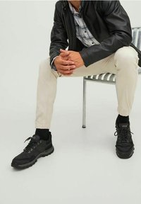 Sneakers neri realizzati in un mix di tessuto e gomma con lacci visibili, ammortizzazione e una suola testurizzata. Indossati con joggers beige e una giacca.