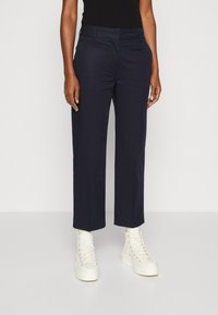 Pantaloni tapered de culoare bleumarin, confecționați dintr-un material neted, cu buzunare frontale și o talie medie, asociați cu adidași albi cu glezna înaltă.