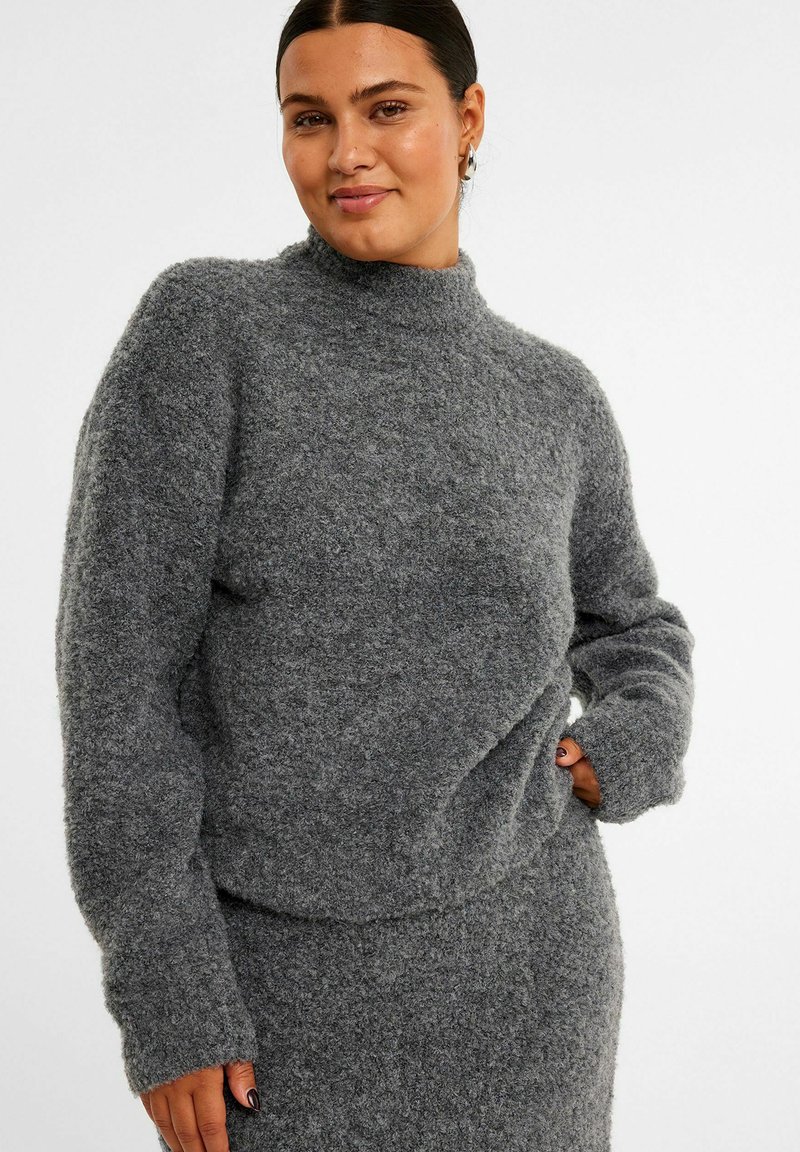 Grå strikket trøje med høj hals og lange ærmer, lavet af et tekstureret, fluffy materiale. Designet er afslappet og let oversized.