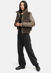 Bruine gewatteerde jas met een fleecesnor, hoge kraag en geribbelde manchetten, gecombineerd met donkere, losse jeans en zwarte sneakers.