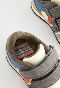 Baskets pour enfants avec des accents bleus, gris et orange, présentant une surface texturée et des sangles Velcro. L'intérieur montre un revêtement en tissu rayé.