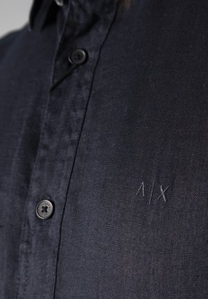 Camicia blu navy con bottoni, realizzata in tessuto testurizzato. Presenta un piccolo logo ricamato "A/X" e un colletto standard con bottoni neri.