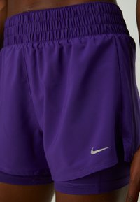 Nærbilde av en person som har på seg lilla Nike treningsshorts med elastisk midje og hvit Nike swoosh-logo på venstre bein.