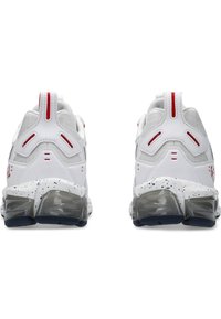 Zapatillas deportivas blancas con parte superior de malla y sintético, acentos rojos, talón texturizado y una media suela moteada; amortiguación gruesa y translúcida.