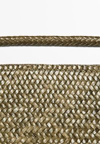 Nærbillede af en tekstureret taske og rem med bronzefarvet flettet læder vævet i et tæt, indviklet mønster.