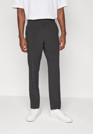 Dark gray tailored trousers made from a textured fabric, featuring a button clasp, side pockets, and a slim fit. Paired with white sneakers.